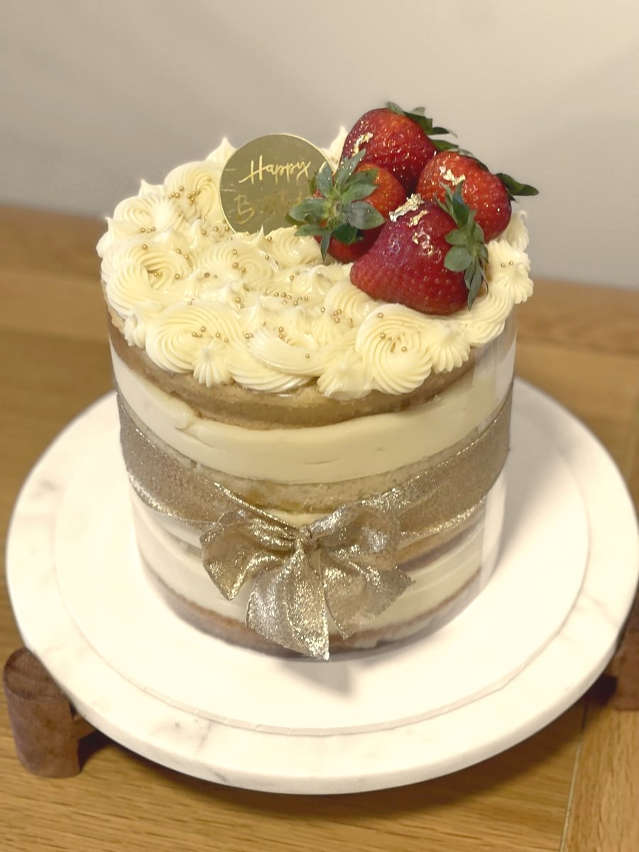 Naked cake with vanilla cream, fresh strawberries and a gold ribbon